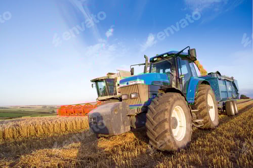Preview: A Low Angle Shot Of A Combine Harvester And A Blue Filling Trailer In A Wheat Field.