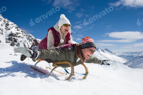 Preview: A Senior Adult Man Lying On A Sled As He Pretends To Fly With His Arms Outstretched While His Wife