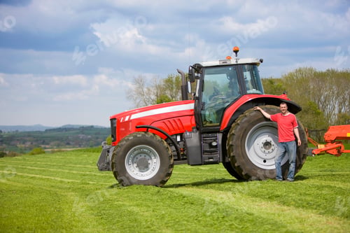 Preview: An Adult Farmer Proudly Standing Next His Giant Red Tractor In A Silage Farm Field On A Bright