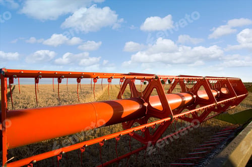 Preview: A Close Up Of Blades Of A Combine Harvester In A Sunny Wheat Field With Clouds In Background.