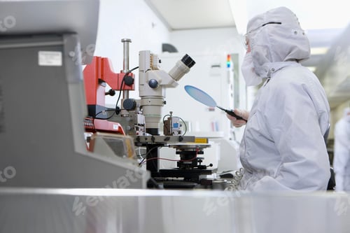 Preview: A Horizontal View Of A Scientist In Clean Suit Examining The Silicon Wafer While Sitting Next To A