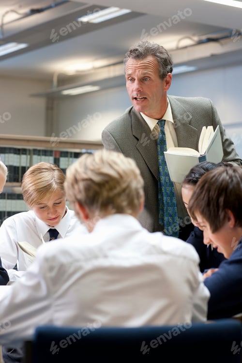 Visualização: Um retrato de um professor lendo para seus alunos sentados juntos em uma mesa redonda em uma escola