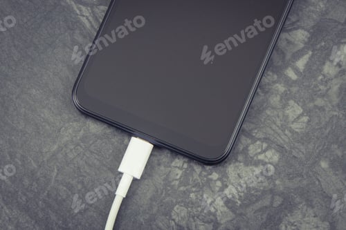 Preview: Black Smartphone With Connected White Plug Of Charger. Telephone Charging