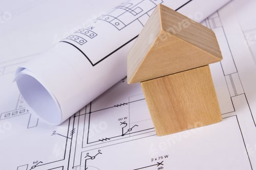Preview: House Shape Made Of Wooden Blocks And Rolls Of Diagrams Lying On Electrical Construction Drawings