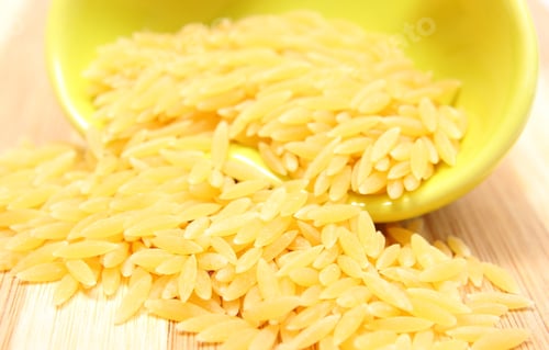 Preview: Closeup Of Yellow Pasta Pouring Out Of Yellow Glass Bowl On Wooden Cutting Board