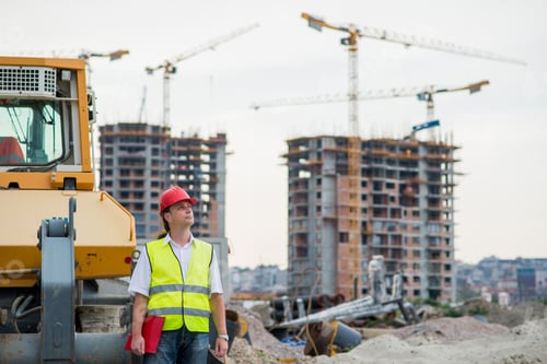 Preview: Engineer In Front Of Excavator On A Construction Site With Buildings And Cranes In The Background