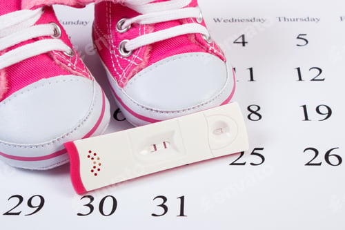 Preview: Pregnancy Test With Positive Result And Baby Shoes Lying On Calendar, Concept Of Extending Family