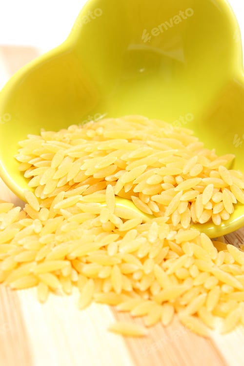 Preview: Closeup Of Yellow Pasta Pouring Out Of Yellow Glass Bowl On Wooden Cutting Board