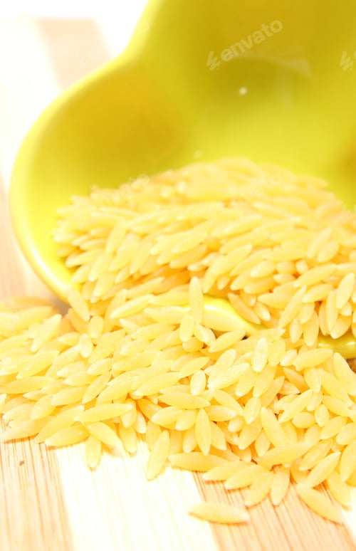 Preview: Closeup Of Yellow Pasta Pouring Out Of Yellow Glass Bowl On Wooden Cutting Board