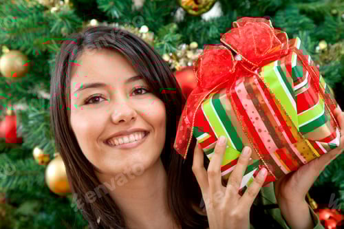 Preview: Smiling Woman Holding Christmas Present by Decorated Tree