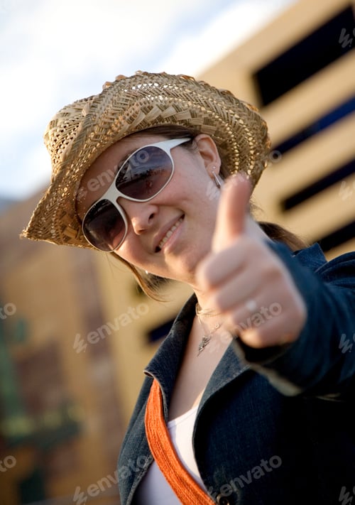 Preview: Female Tourist With Thumbs Up Wearing A Hat Outdoors