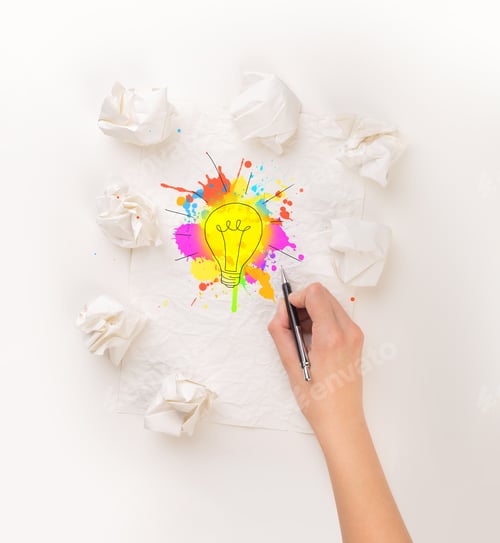 Preview: Female Hand Next To A Few Crumpled Paper Balls Drawing A Colorful Lightbulb
