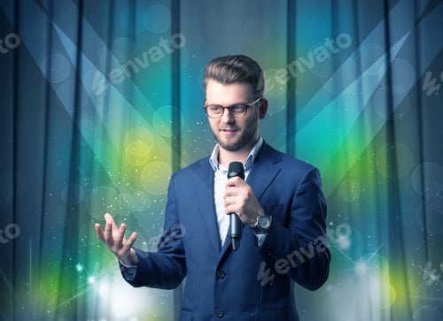 Preview: Businessman Speaking Into Microphone With Blue Curtain Behind Him