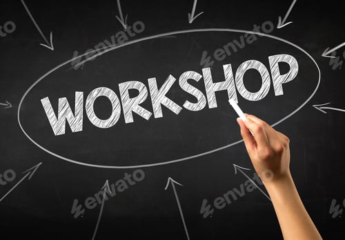 Preview: Female Hand Holding White Chalk In Front Of A Blackboard With Workshop Written On It