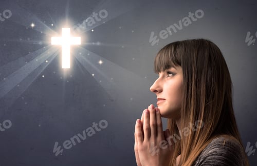 Preview: Young Woman Praying On A Grey Background With A Shiny Cross Above Her
