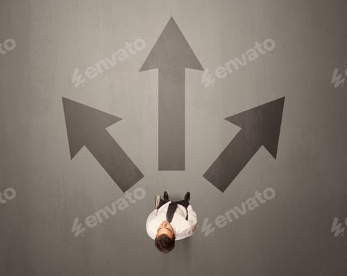 Preview: Young Contemplating Businessman Stands In Front Of Brown Arrows