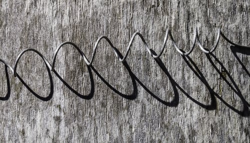 Preview: Metal Coil With Parabolic Shadows Cast By Sunlight On Weathered Wood