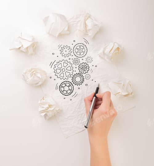 Preview: Female Hand Next To A Few Crumpled Paper Balls Drawing Rotating Gears