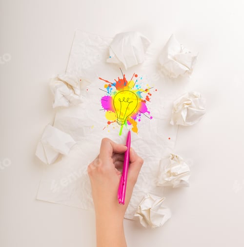 Preview: Female Hand Next To A Few Crumpled Paper Balls Drawing A Colorful Lightbulb