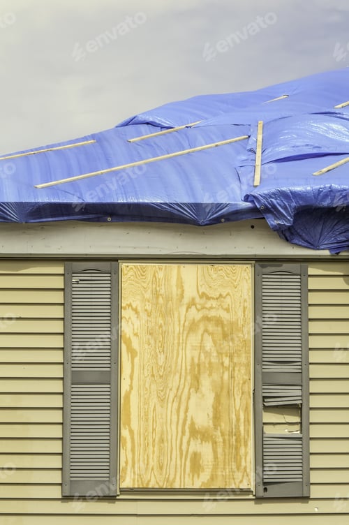 Preview: House Repairs After Tornado: Boarded Window Beneath Roof With Protective Sheets Of Blue Plastic