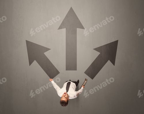 Preview: Young Contemplating Businessman Stands In Front Of Brown Arrows