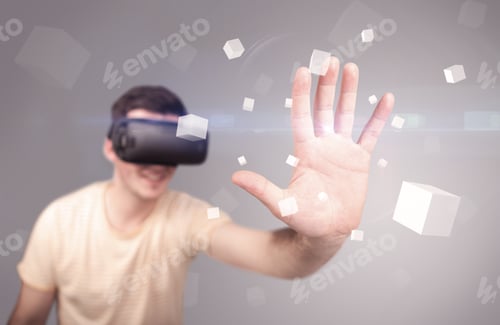 Preview: Young Impressed Man Wearing Virtual Reality Goggles With Grey Cubes Around Him