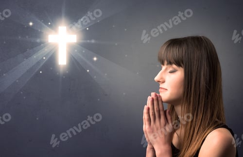 Preview: Young Woman Praying On A Grey Background With A Shiny Cross Above Her