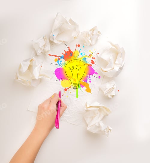 Preview: Female Hand Next To A Few Crumpled Paper Balls Drawing A Colorful Lightbulb