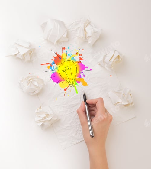 Preview: Female Hand Next To A Few Crumpled Paper Balls Drawing A Colorful Lightbulb