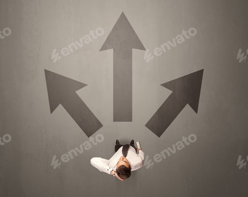 Preview: Young Contemplating Businessman Stands In Front Of Brown Arrows