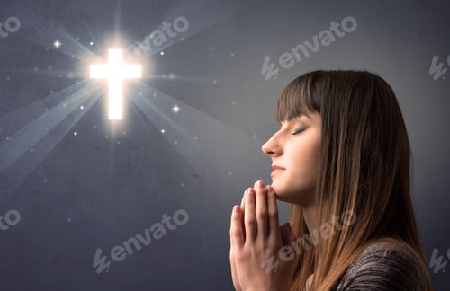 Preview: Young Woman Praying On A Grey Background With A Shiny Cross Above Her