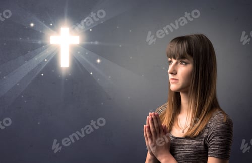 Preview: Young Woman Praying On A Grey Background With A Shiny Cross Above Her