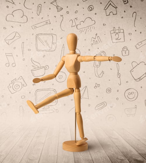 Preview: Wooden Mannequin Posed In Front Of A Greyish Background With Mixed Media Scribbles Behind It