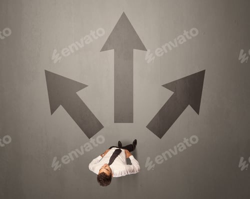 Preview: Young Contemplating Businessman Stands In Front Of Brown Arrows