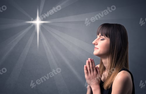 Preview: Young Woman Praying On A Grey Background With A Shiny Cross Silhouette Above Her