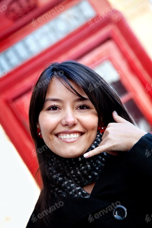 Preview: Woman Standing In Front Of A Telephone Box Doing A Call Me Gesture