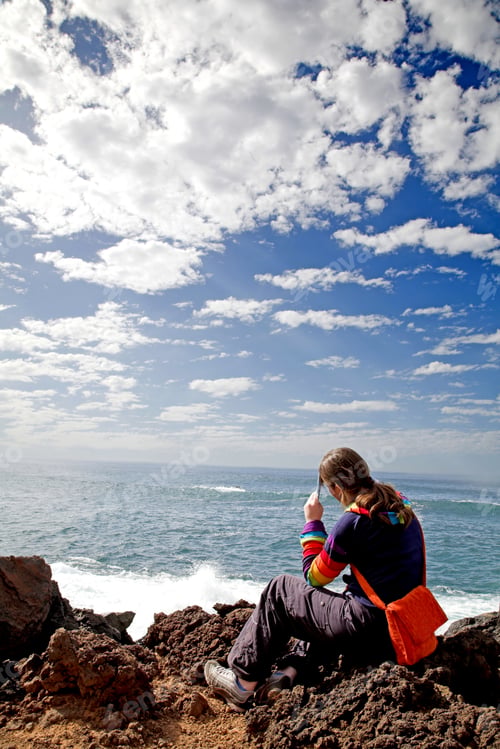 Preview: Pensive Woman By The Sea On The Rocks On A Sunny Day With A Blue Sky