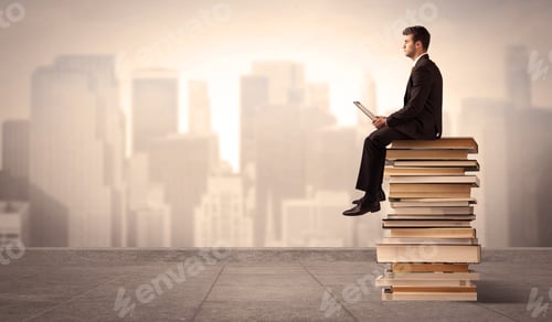 Preview: A Serious Businessman With Laptop Tablet In Elegant Suit Sitting On A Stack Of Books In Front Of
