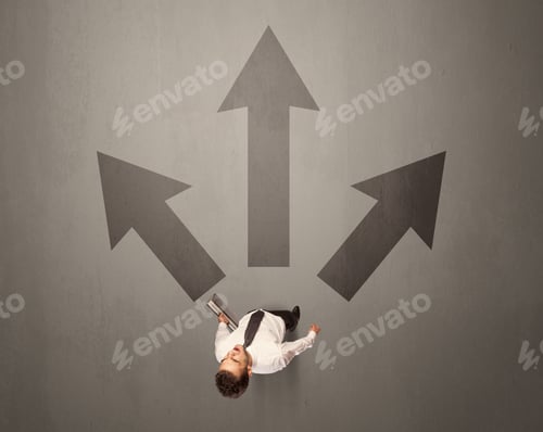 Preview: Young Contemplating Businessman Stands In Front Of Brown Arrows