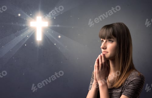 Preview: Young Woman Praying On A Grey Background With A Shiny Cross Above Her