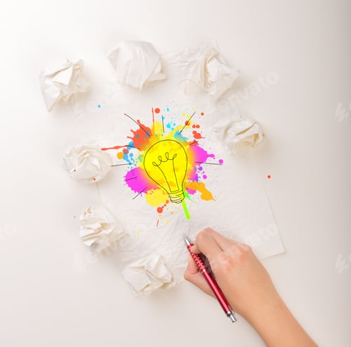 Preview: Female Hand Next To A Few Crumpled Paper Balls Drawing A Colorful Lightbulb
