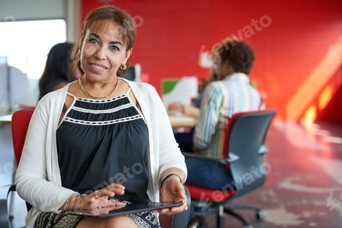 Preview: Confident Female Boss Working On A Digital Tablet In Red Creative Office Space