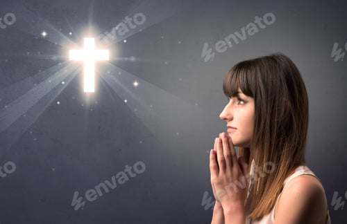 Preview: Young Woman Praying On A Grey Background With A Shiny Cross Above Her