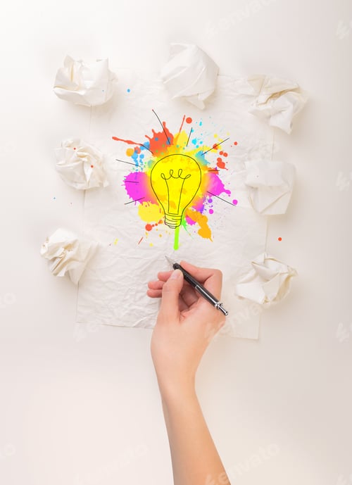 Preview: Female Hand Next To A Few Crumpled Paper Balls Drawing A Colorful Lightbulb
