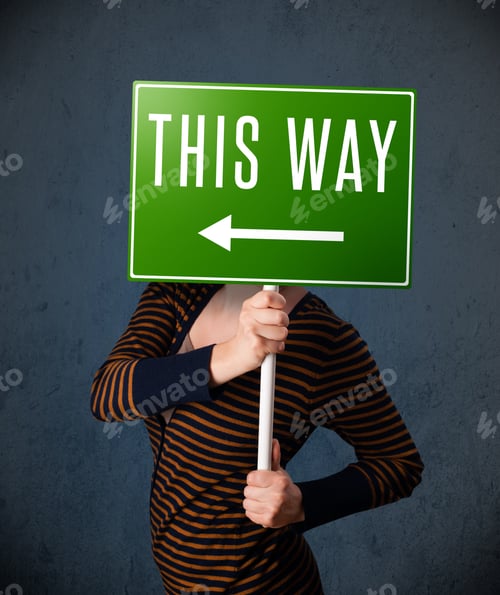 Preview: Young Lady Standing And Holding A Green Direction Sign In Front Of Her Head