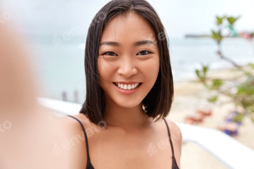 Preview: Pretty Young Asian Woman Takes Photo On Camera Og Unrecognizable Gadget, Poses Against Sea Or Ocean