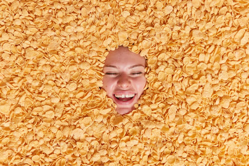 Preview: Joyful Woman Smiles Happily Keeps Eyes Closed Being In Good Mood Buried In Cornflakes Feels Very