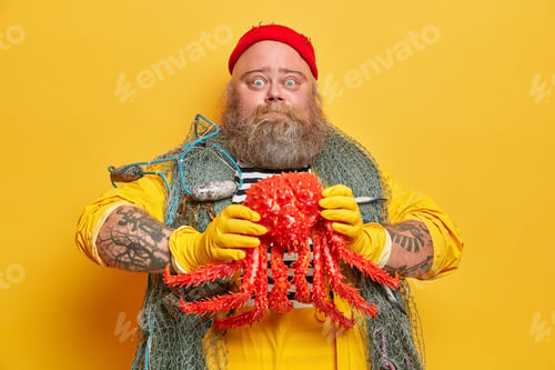 Preview: Bearded Plump Fisherman Wears Striped Jumper And Overalls Holds Big Red Octopus In Hands Works On