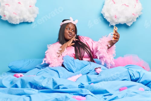 Preview: Attractive Dark Skinned Chubby Lady Pouts Lips At Smartphone Camera Makes Selfie Portrait Wears