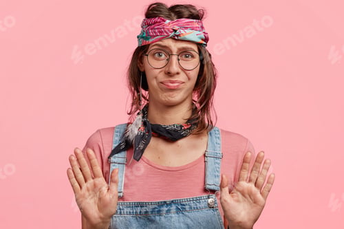 Preview: Beautiful Hippie Girl Poses Against Pink Background, Makes Stop Gesture, Has Displeased Expression